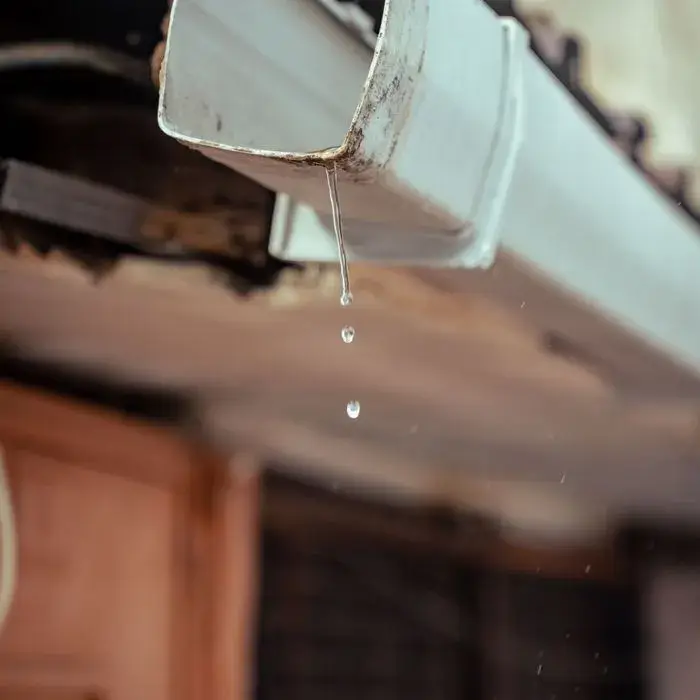 A leaking gutter joint dripping water below the roofline