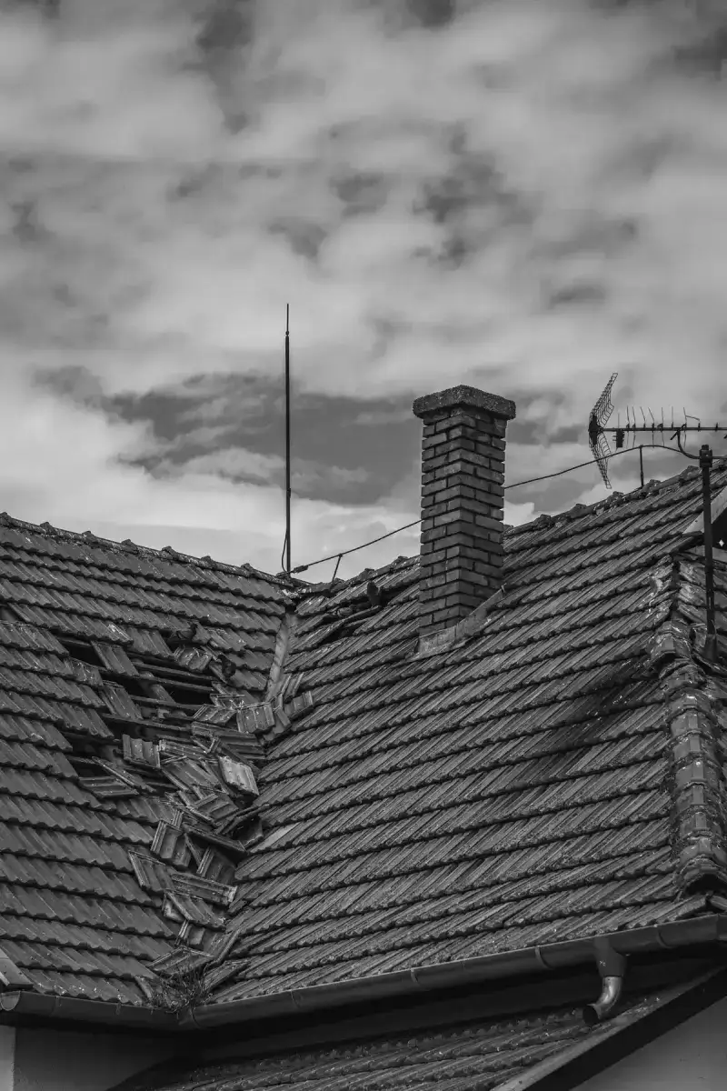 A tile roof with storm damage — broken tiles near the chimney, shown in black and white