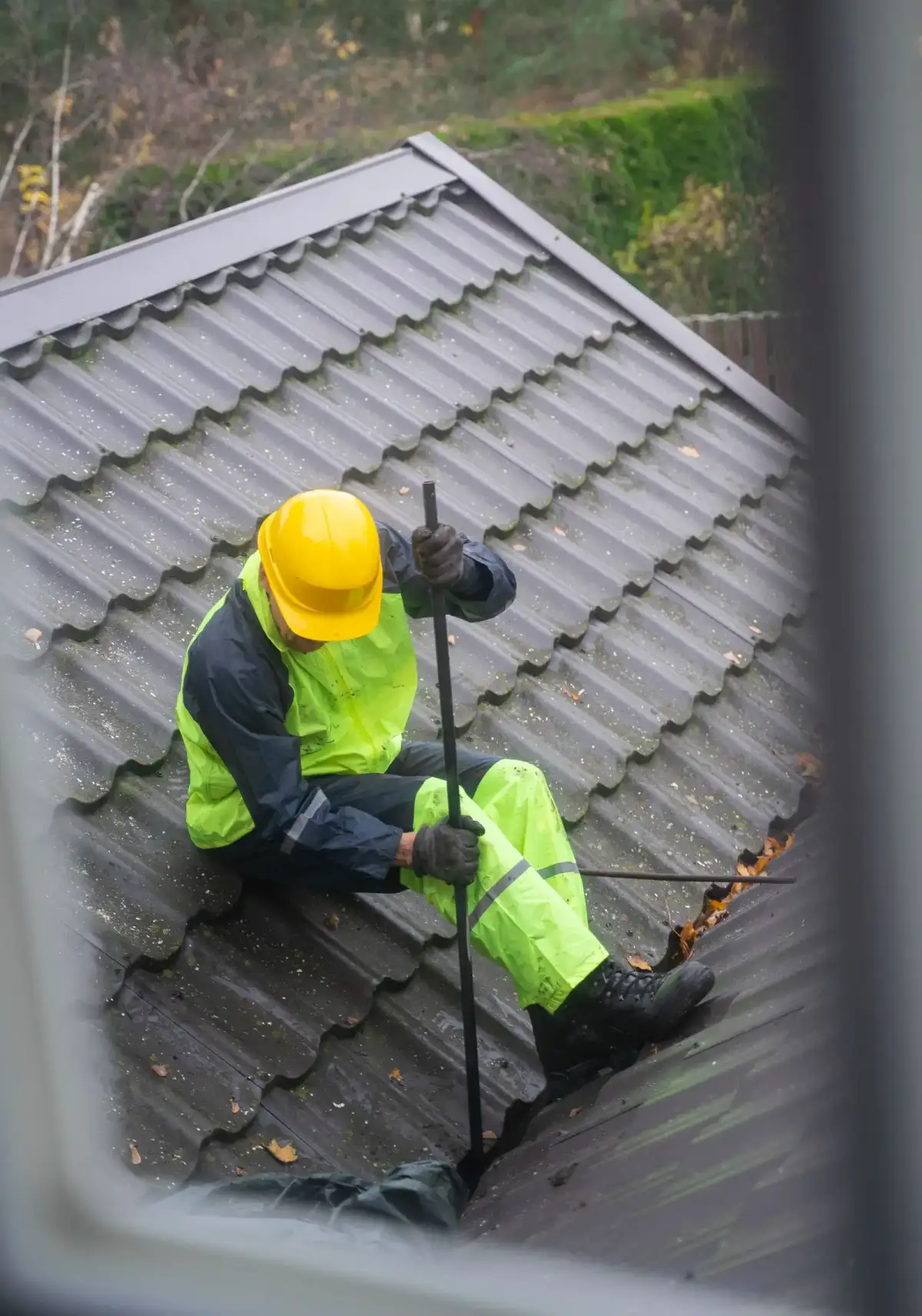 A worker in safety gear cleaning a rain gutter on a roof